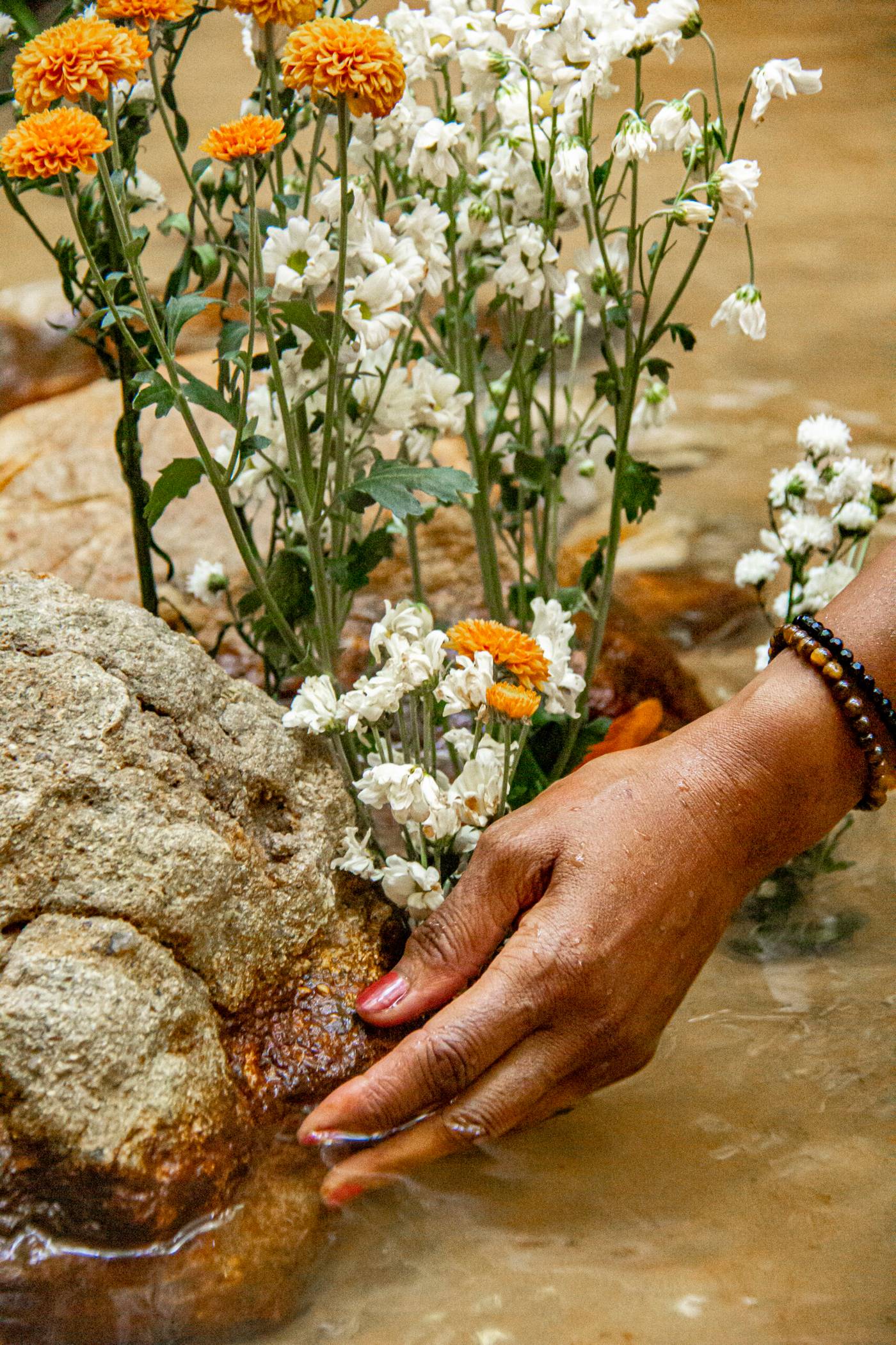 Mano colocando una ofrenda de flores blancas y naranjas en el agua de la cascada